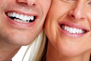 A close-up of a man and a woman smiling side-by-side, showcasing healthy, straight white teeth.