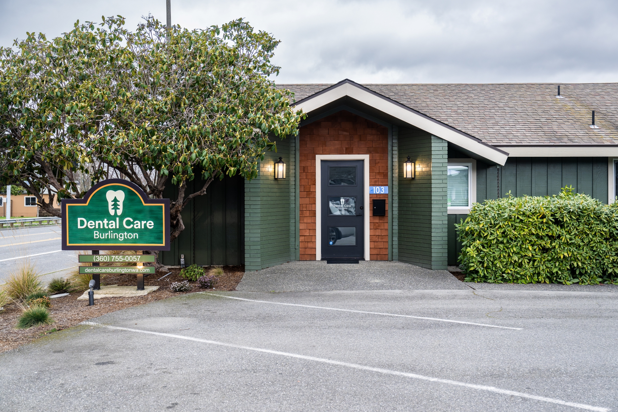 View of the office from the parking lot - small green building with cedar shingles around the front door